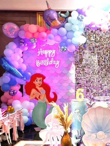 The main photo backdrop featuring a large Ariel cutout, a neon "Happy Birthday" sign, and a beautiful balloon arch with foil sea creature balloons.