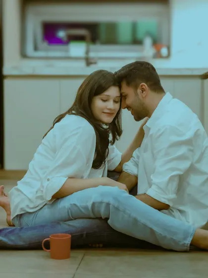 An intimate and cozy at-home style shoot, with a couple sitting on the floor of a modern kitchen, sharing a tender moment.