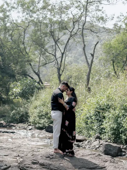 A wide shot of a couple sharing an intimate moment in a lush, green landscape. This pre-wedding photo emphasizes the beauty of nature as a backdrop for their love story.