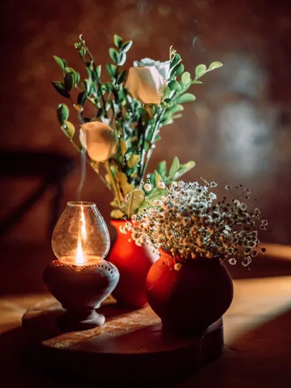 A close-up of a rustic table centerpiece, combining an earthen lamp, simple vases, and delicate flowers to create a warm and intimate ambiance.