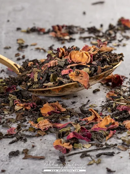 A macro photograph of premium tea leaves on a golden spoon. This close-up highlights the intricate details and quality of the blend, justifying a premium price point.