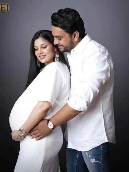 A classic couple's pose against a dark studio background. The focus is on their connection and the beautiful baby bump.