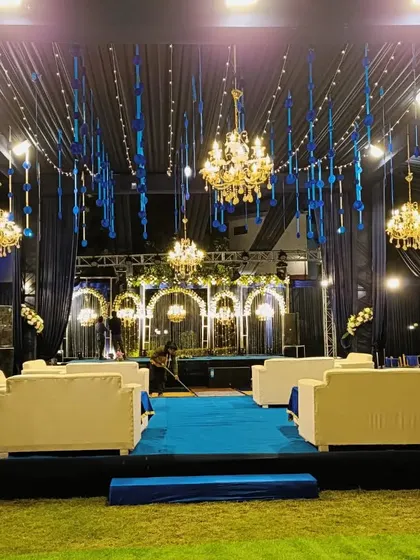 A grand outdoor engagement setup in a striking blue and white theme, with a canopy of blue ribbons and crystal chandeliers.