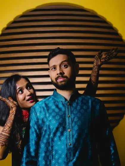 A playful couple portrait from a Mehendi celebration. The bride's henna-covered hands framing the groom's surprised face makes for a fun and memorable shot.