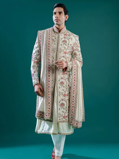 An off-white sherwani featuring exquisite, multi-colored floral embroidery that cascades down the front and sleeves. This piece, complete with a matching stole, is a wearable work of art for a day wedding.