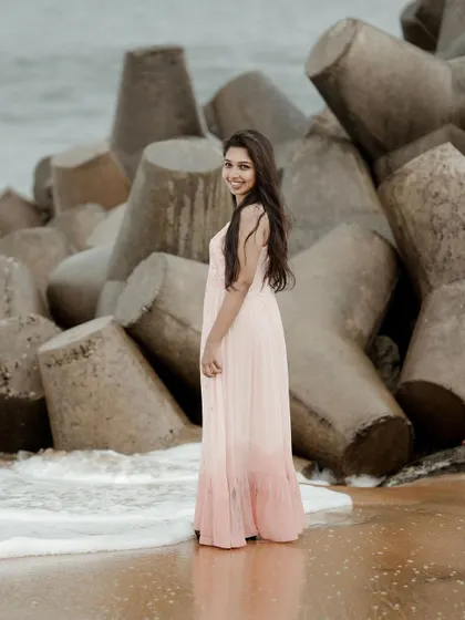 A full-length portrait on the beach, with the waves and sea rocks creating a dramatic natural backdrop. Her pose is elegant and effortless, perfect for a lifestyle or fashion shoot.