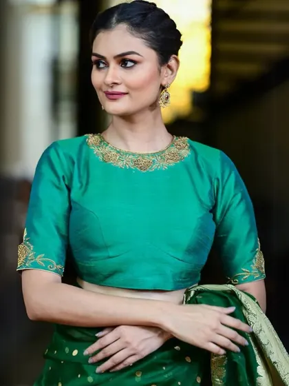 This emerald green raw silk blouse features delicate gold embroidery around the boat neckline and on the sleeves. It's a classic, elegant choice for weddings and formal events.