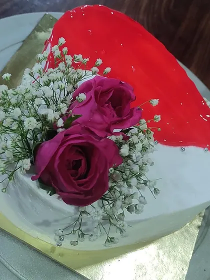 A heart-shaped cake that's both romantic and artistic. It features a striking red glaze over one half and is beautifully decorated with fresh pink roses and baby's breath.