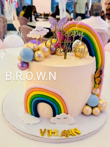 A beautiful rainbow and butterfly themed cake. The design features two fondant rainbows, shimmery gold and blue spheres, and delicate butterflies.