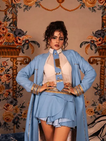 A powerful, direct-to-camera shot showcasing the sharp makeup and curly updo created for this high-fashion look.