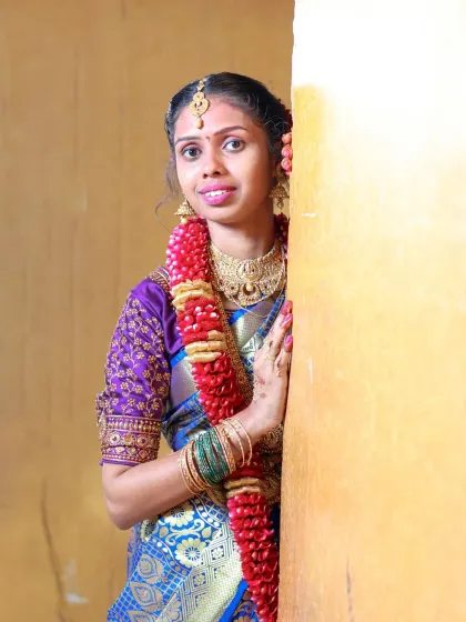 An indoor portrait from a puberty ceremony. The simple, warm-colored wall provides a clean background that makes the subject's detailed saree and jewelry the main focus.