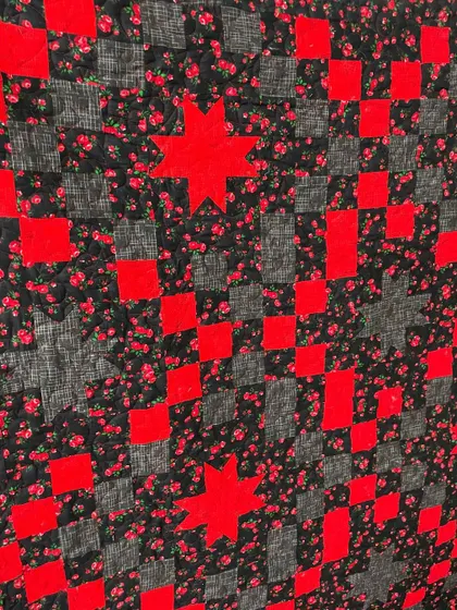 A close-up of a star quilt, showing the quilting on the high-contrast red and black fabrics.