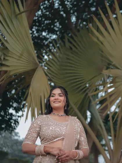 A low-angle shot of the bride, Pallavi, standing majestically under palm trees. This portrait gives her a powerful and elegant presence.