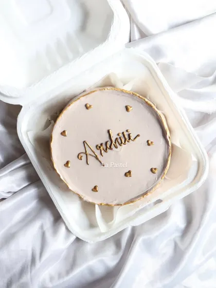 A personalized bento cake with the name 'Archii' in beautiful gold calligraphy, edged with a gold rim and hearts.