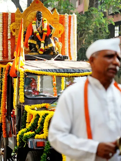 A devotee walks alongside the decorated float of Chhatrapati Shivaji Maharaj. This image captures the blend of devotion and tradition that characterizes the Shobha Yatra.
