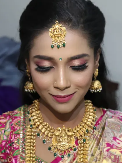 A close-up of a South Indian bride's makeup. The focus is on the shimmery pink and gold eye makeup, which adds a touch of modern glam to the traditional look, paired with temple jewellery and a pink silk saree.