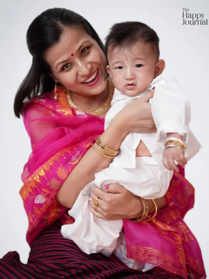 A mother dressed in a vibrant pink saree holds her baby, who is dressed in traditional white. A beautiful portrait celebrating culture and motherhood.