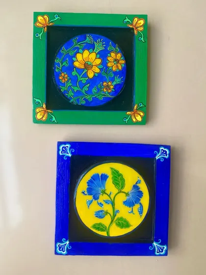 A pair of the framed floral pieces, showing the vibrant blue and green frames and the contrasting floral designs within.