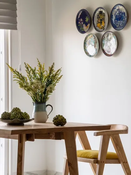An angled shot of the dining table, showing the beautiful grain of the wood and the collection of decorative wall plates. The space feels both modern and warm, perfect for everyday meals.