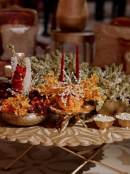 A detail shot of a coffee table centerpiece, featuring brass bowls with floating flowers and candles. These small touches add to the warm, traditional, and celebratory feel of the event.