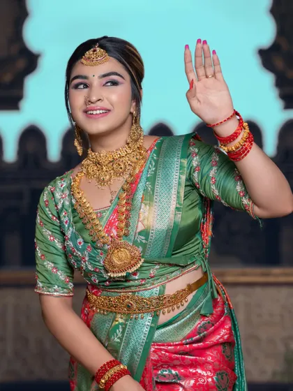 A model waves happily, dressed in a green and red half saree and a full set of our antique gold rental jewellery.