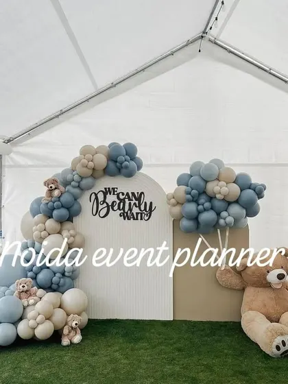 A 'We Can Bearly Wait' baby shower setup inside a tent, using muted blue and beige balloons and wooden 'BABY' blocks for a clean, modern look.