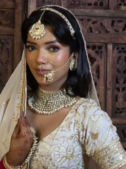 An elegant bride in a white and gold lehenga, wearing a simple but beautiful pearl choker set. This is a great choice for a minimalist bride.