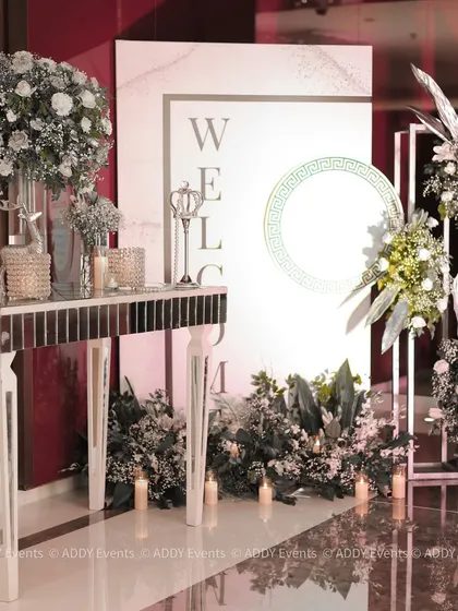 We design exquisite welcome areas to greet your guests in style. This setup includes a mirrored console table, lush floral arrangements, elegant candles, and a custom welcome sign, creating a luxurious first impression.