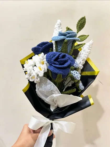 A bold and beautiful custom bouquet featuring deep blue crochet roses paired with delicate white filler flowers. The contrast with the black and gold wrapping paper creates a dramatic and sophisticated look.