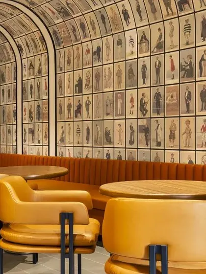 A vibrant cafeteria at the Carlsberg office, featuring custom wallpaper depicting historical brand imagery. The curved banquette seating and warm tones create a social and engaging atmosphere for employees to relax and connect.