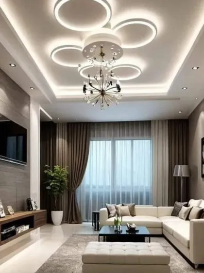 We designed this living room with a focus on ceiling aesthetics, featuring a modern, multi-ring chandelier and cove lighting. The neutral-toned sectional and dark wood media console create a balanced and contemporary look, perfect for both relaxing and entertaining.