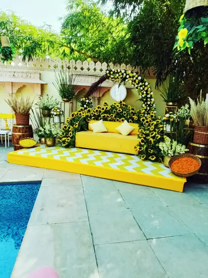 A chic poolside Haldi setup with a yellow sofa on a chevron stage, framed by sunflowers and lush greenery.