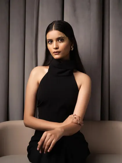 A direct, seated portrait against a simple curtain backdrop. This classic setup allows the model's presence and the elegant black dress to be the main focus.