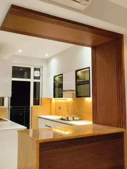 A custom wooden breakfast counter serves as a beautiful and practical partition, connecting the kitchen to the living area. This design element adds a natural, warm touch to the modern kitchen setup.