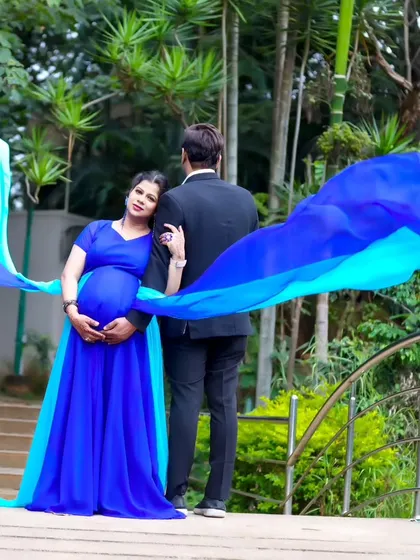 A romantic rear-view shot of a couple on a bridge, with the blue trail of the maternity gown flowing beautifully.