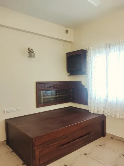 A wider view of the guest bedroom, showing the queen-size bed with movable under-cot storage on wheels. The room is sparsely furnished to allow space for the client's mother to practice her music.