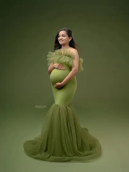A simple, elegant full-length portrait against a solid olive green background. This classic shot puts all the focus on you, your baby bump, and the beautiful flow of the gown.