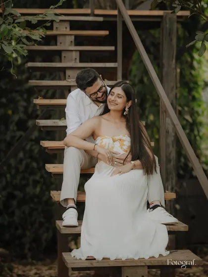 A sweet pre-wedding portrait on a rustic wooden staircase. The groom rests his head on the bride's shoulder as she smiles, a picture of comfort and love.