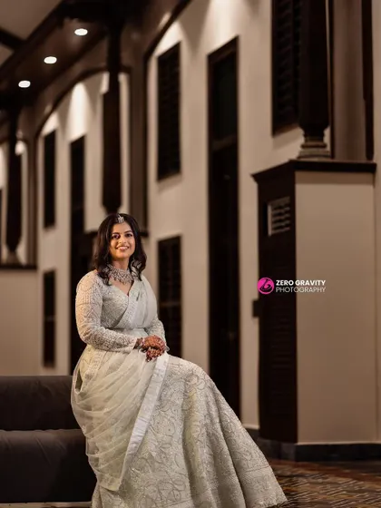 A simple and elegant reception look. The bride is seated, looking serene in her beautiful white lehenga, with makeup that enhances her natural grace.