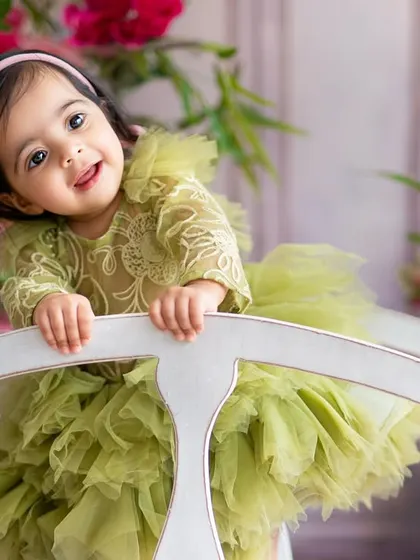 Peeking over a chair with a sweet smile, this little one is the star of her floral-themed first birthday shoot. We use various props to create diverse and playful portraits.