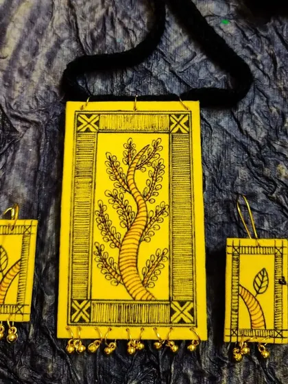 A hand-painted fabric necklace featuring a 'tree of life' motif in the Madhubani style. The ghungroo bells at the bottom add a gentle sound and movement.