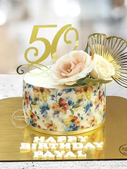 A stunning 50th floral cake with a printed floral wrap. The design is topped with fresh flowers and a golden "50" for an elegant touch.