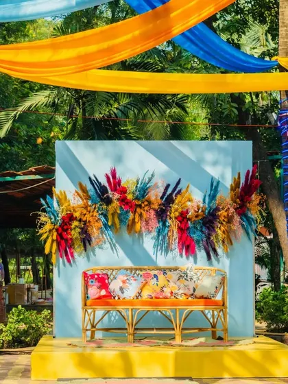 This photo shows a dedicated photo spot with a cane bench set against a light blue wall, decorated with a beautiful multi-colored pampas grass installation.