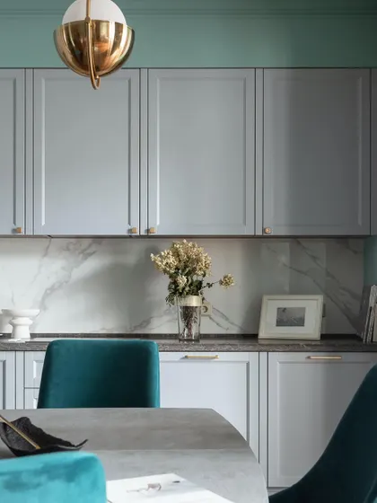 A close-up of a modern dining area, showing PU-finish light grey kitchen cabinets that double as a crockery unit, paired with plush teal velvet chairs.