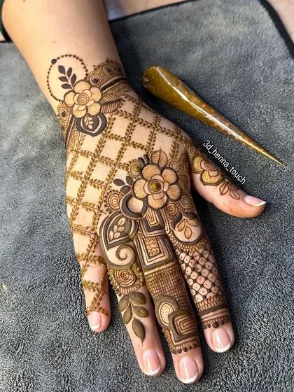 A beautiful floral design with a net pattern on the palm. The henna cone is placed next to the hand, showing the tool of our trade.