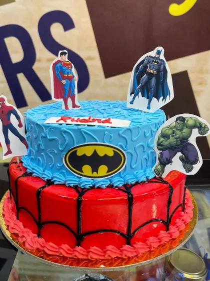 A 2.5kg two-tiered superhero cake featuring logos and characters from the Avengers and DC universes.