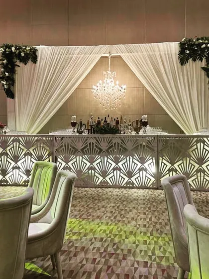 An elegant bar setup for a Roka ceremony, with a backlit art deco-style facade, a crystal chandelier, and simple floral accents.