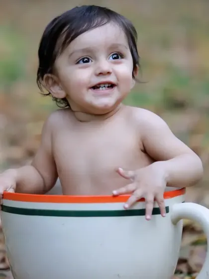 A happy baby boy with a big smile, posing in our giant teacup prop during an outdoor session among autumn leaves.