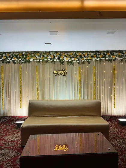 The full view of the elegant Haldi stage with a simple sofa and a beautifully decorated backdrop. The focus is on clean lines and subtle floral accents.