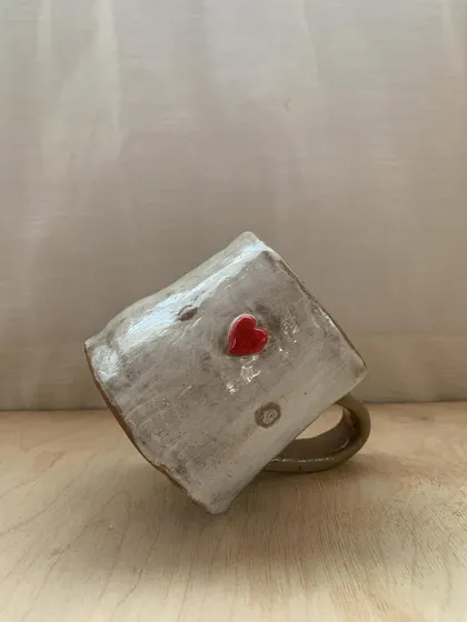 A rustic, heart-adorned mug made by a student, tilted to show its unique character. This piece tells a story of learning, patience, and the love of making.